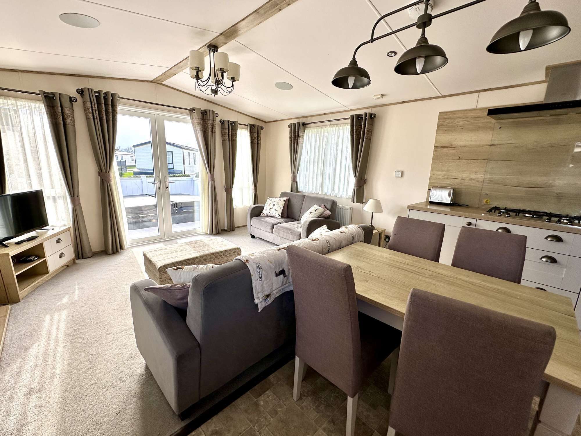 A modern living room with a sofa, dining table, and chairs, a TV, and a kitchen area with a stove.