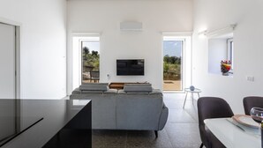En moderne stue med en grå sofa, et fladskærms-tv og et spiseområde med bord og stole.