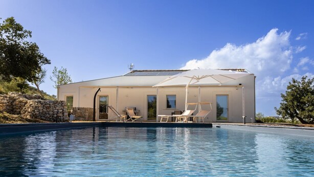 Et moderne hus med swimmingpool, udendørs møbler og en stenvæg.