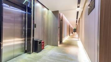 A hotel corridor with elevators, a trash bin, and a sign on the wall.