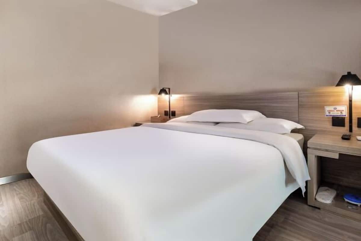 A hotel room with a bed, bedside tables, and wall-mounted lamps.