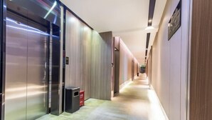 A modern hotel corridor with an elevator, a trash bin, and a long hallway with doors on the right. - Rest Comfort Hotel (Wenzhou Lucheng) (Wenzhou)