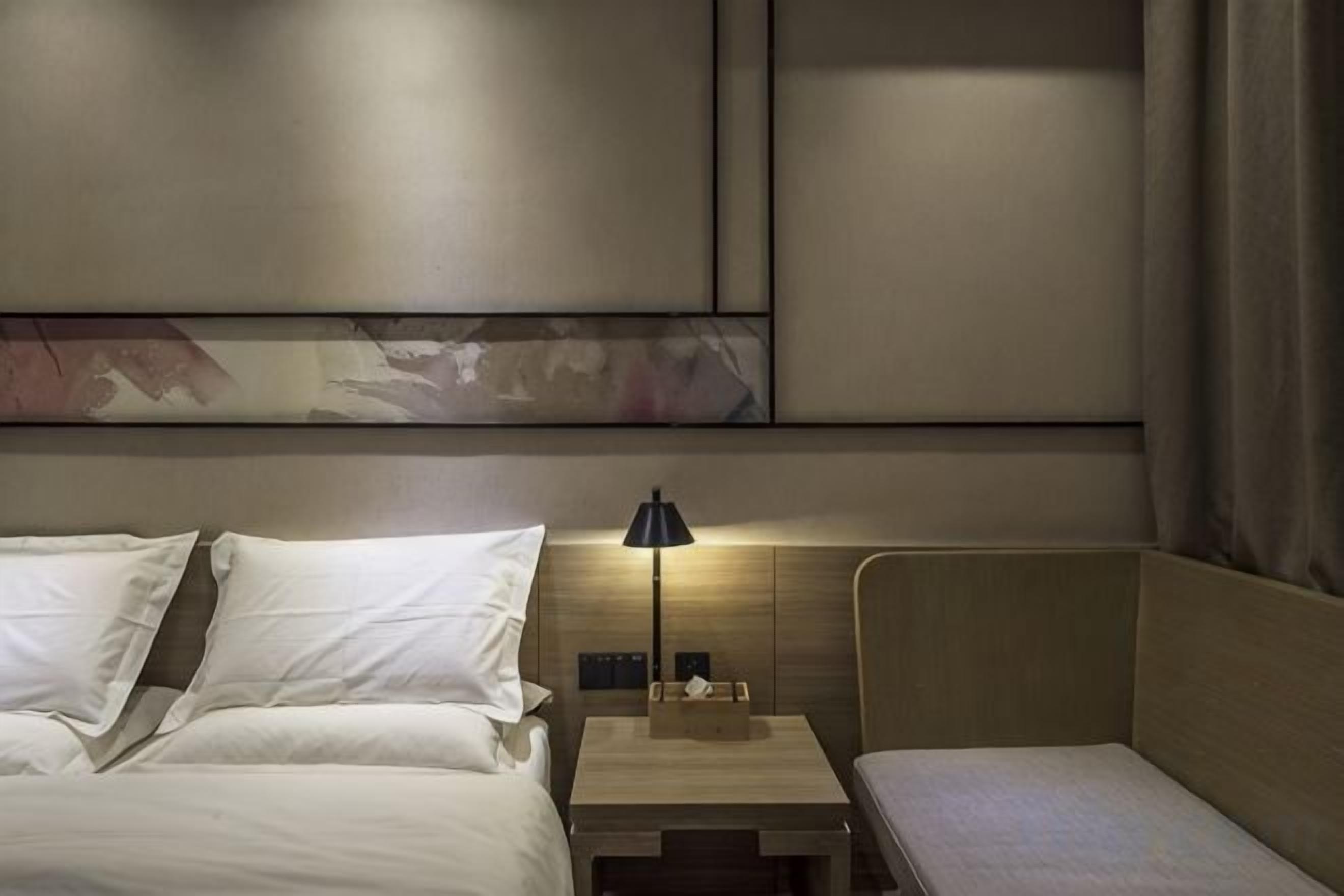 A hotel room with a bed, bedside table, lamp, and a wall-mounted artwork.