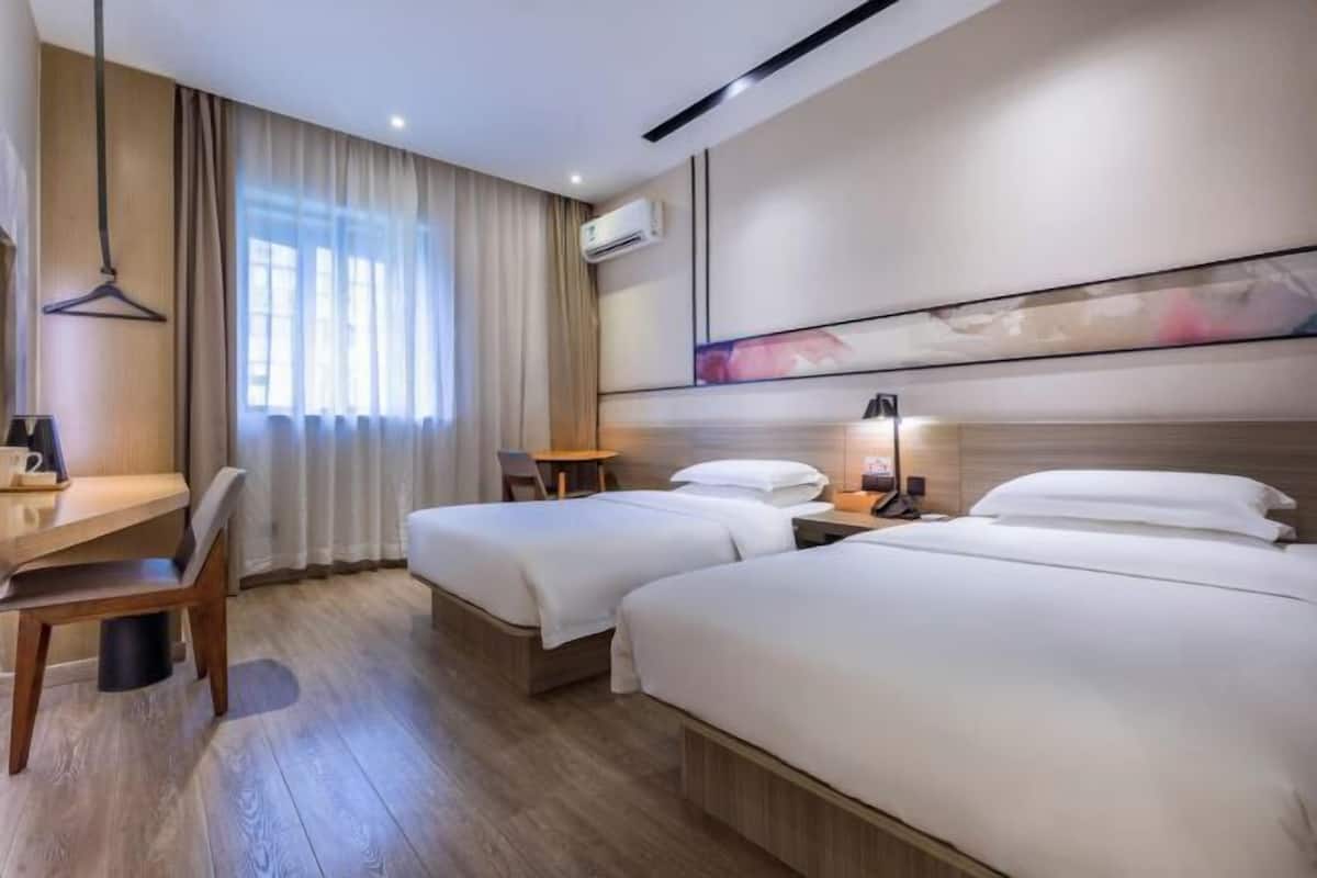 A hotel room with two beds, a desk, a chair, and a hanging light.