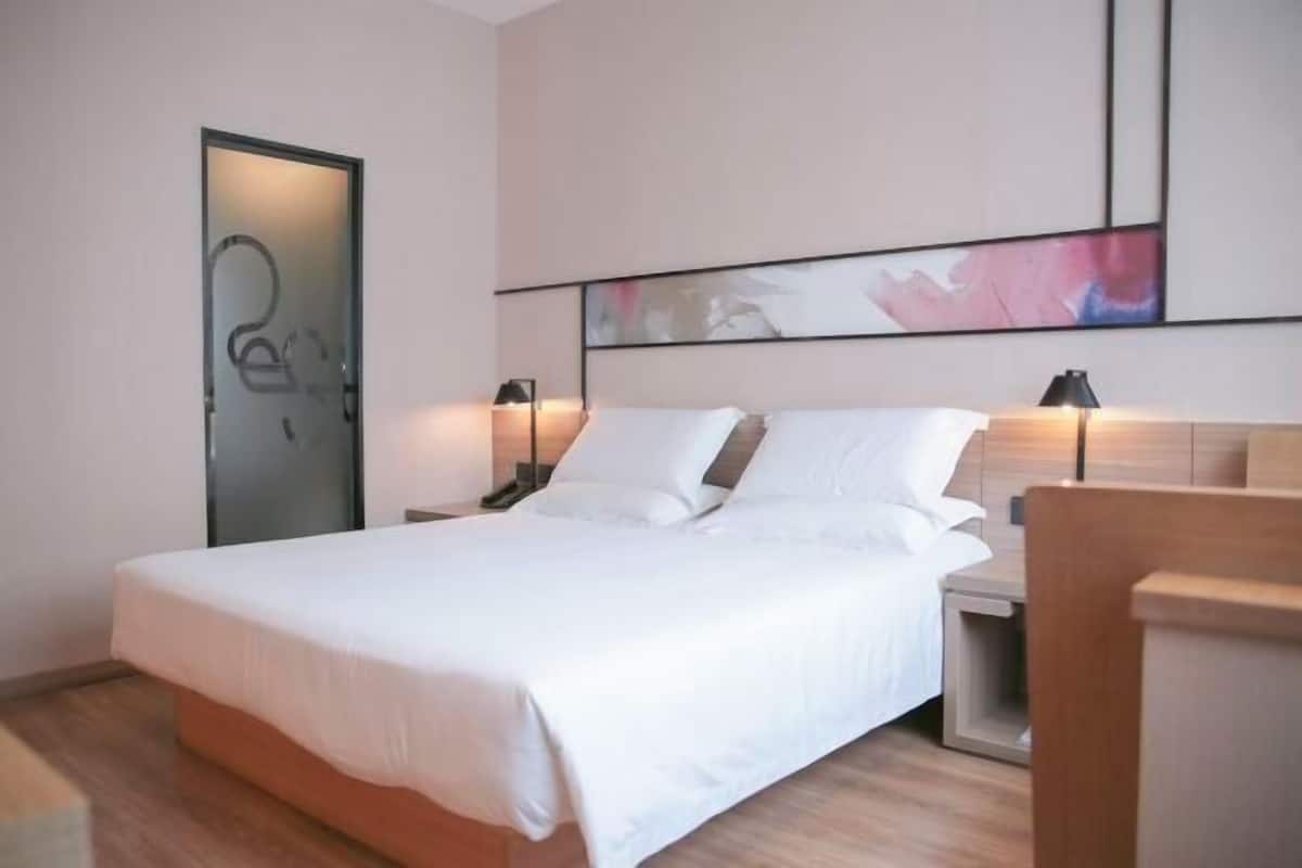 A modern hotel room with a large bed, two bedside tables, a nightstand, and a wooden headboard.