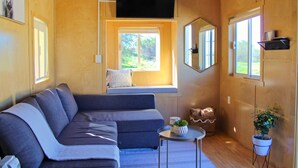 A cozy living room with a grey sofa, a small round table, a potted plant, and a window with a view of greenery. - Rancho Dominique Valle de Guadalupe (Valle de Guadalupe)