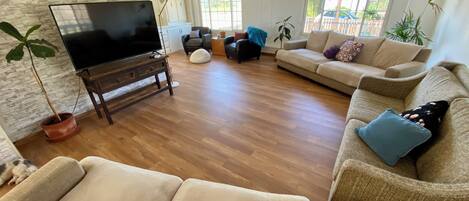 A spacious living room with a large flat-screen TV, multiple sofas, a coffee table, and a potted plant.