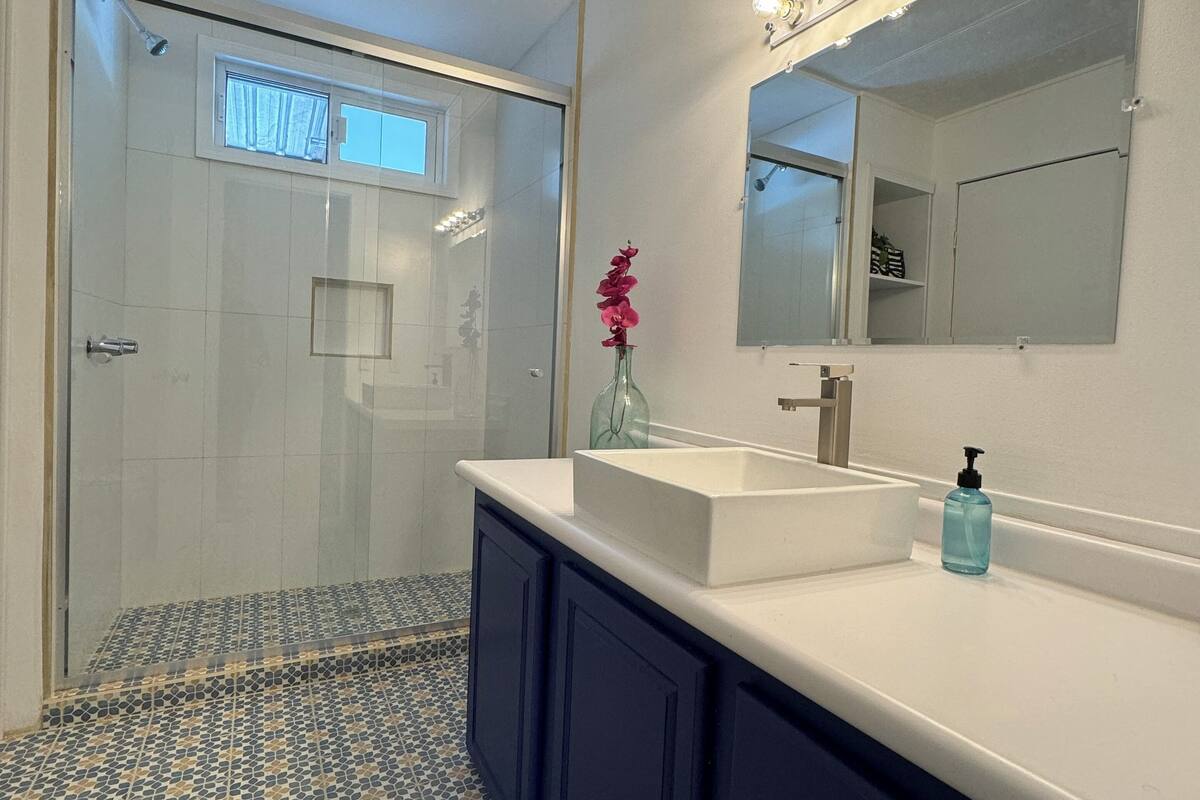 A modern bathroom with a large mirror, a white sink, and a shower area.