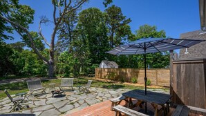 Une terrasse avec un sol en pierre, des meubles en bois et un grand parasol.