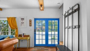 Une pièce avec une porte bleue, un plancher en bois, un banc, une table avec un panier, un rideau jaune et un porte-objets fixé au mur.