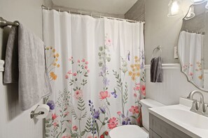 A bathroom with a floral shower curtain, a white sink, and a mirror. - Walk Downtown From Wonderland! (Columbia)