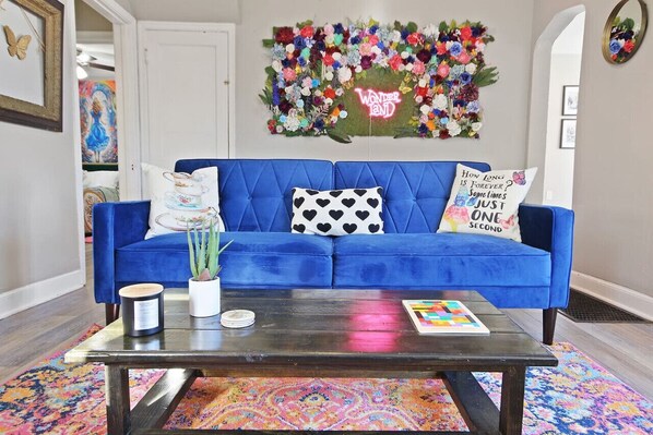 A blue sofa with heart-patterned pillows, a small table with a candle and a plant, and a colorful rug. - Walk Downtown From Wonderland! (Columbia)