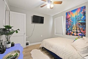 A bedroom with a bed, ceiling fan, TV, and a colorful painting on the wall. - Walk Downtown From Wonderland! (Columbia)