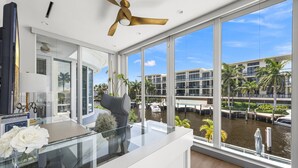 A modern interior with a glass table, a ceiling fan, and a view of a water body and buildings outside. - Villa Seminole: Luxurious Waterfront Retreat with Pool, Gym & Hot Tub (Fort Lauderdale)