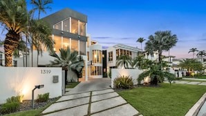 A modern two-story house with a well-maintained lawn and palm trees, featuring a large glass window and a visible address number. - Villa Seminole: Luxurious Waterfront Retreat with Pool, Gym & Hot Tub (Fort Lauderdale)