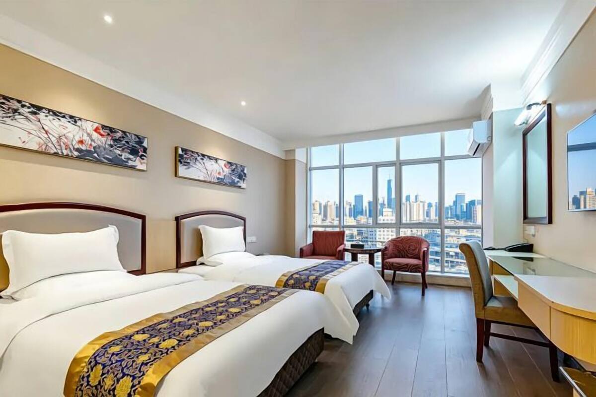 A hotel room with two beds, a desk, and a view of a cityscape.