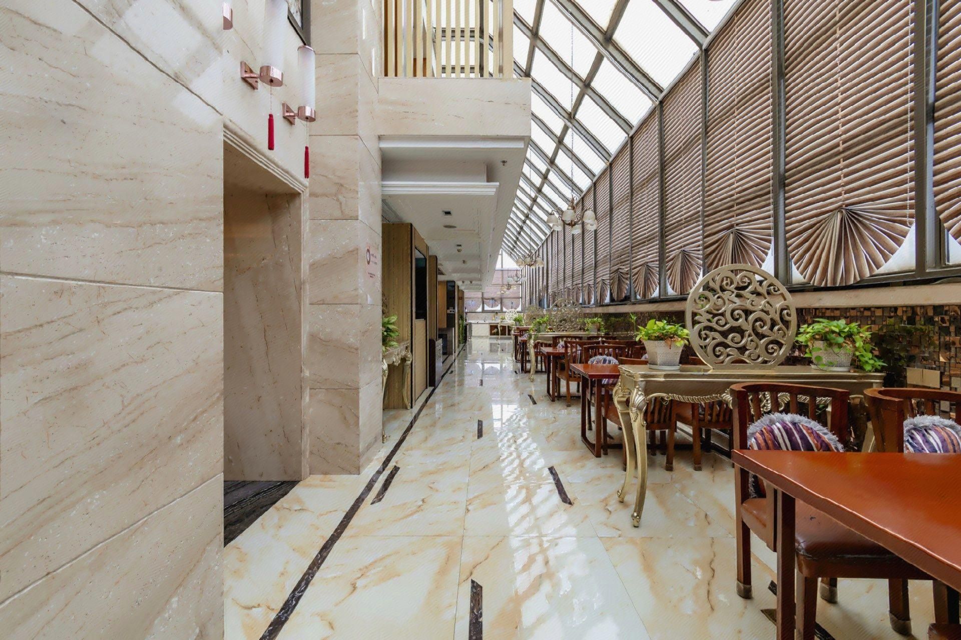 A spacious indoor area with marble flooring, wooden tables and chairs, and a high ceiling with a skylight.