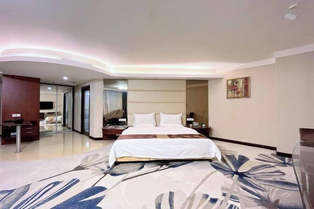A hotel room with a bed, bedside tables, a mirror, and a large floral carpet.