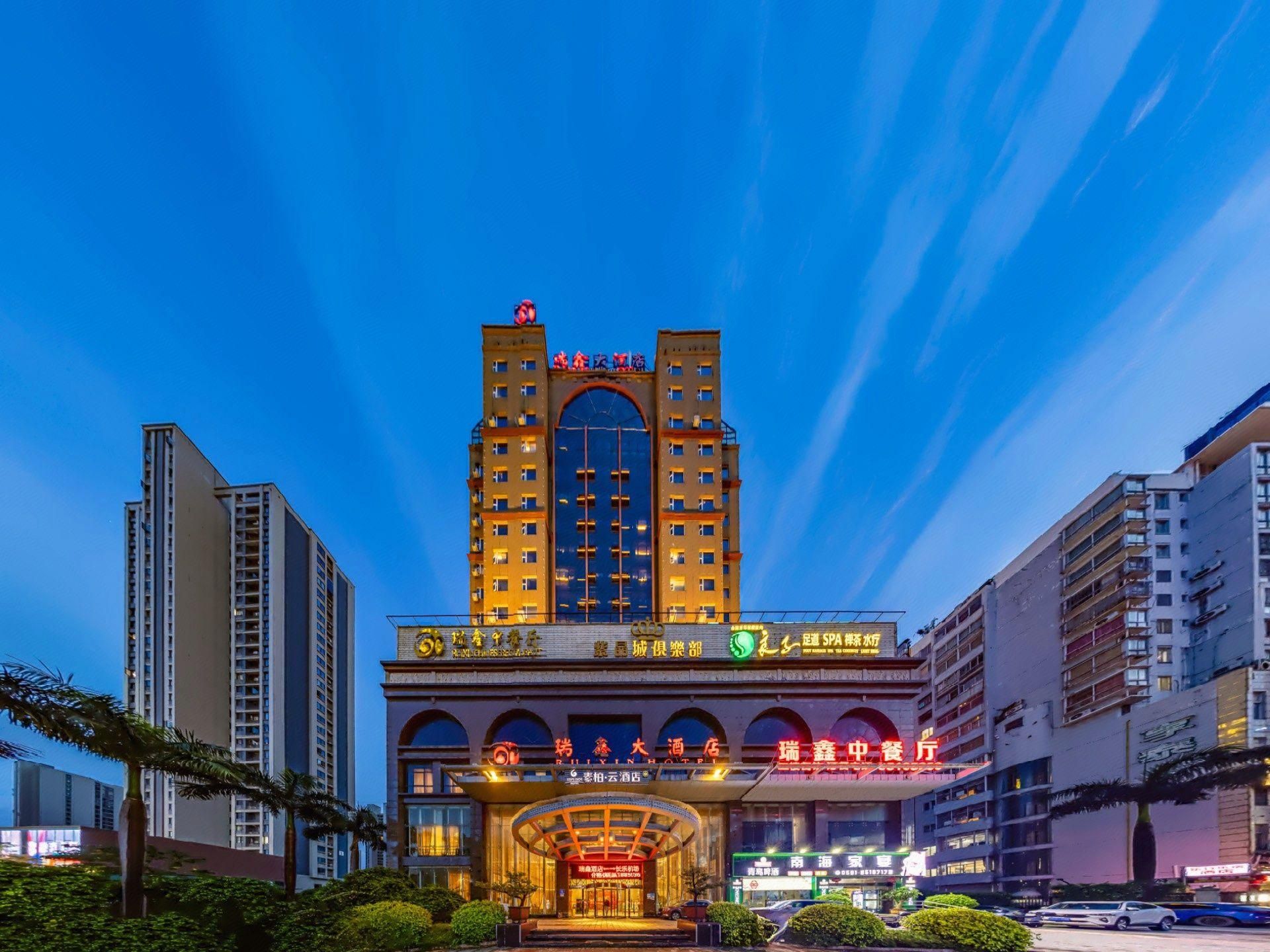 A multi-story hotel with a prominent central tower, multiple balconies, and a well-lit entrance.