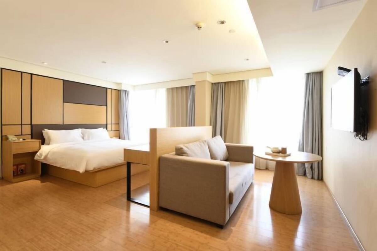 A modern hotel room with a large bed, a sofa, a small table, and a TV mounted on the wall.