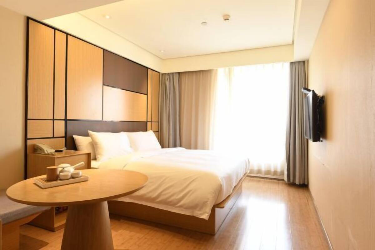 A hotel room with a bed, bedside table, and a TV mounted on the wall.