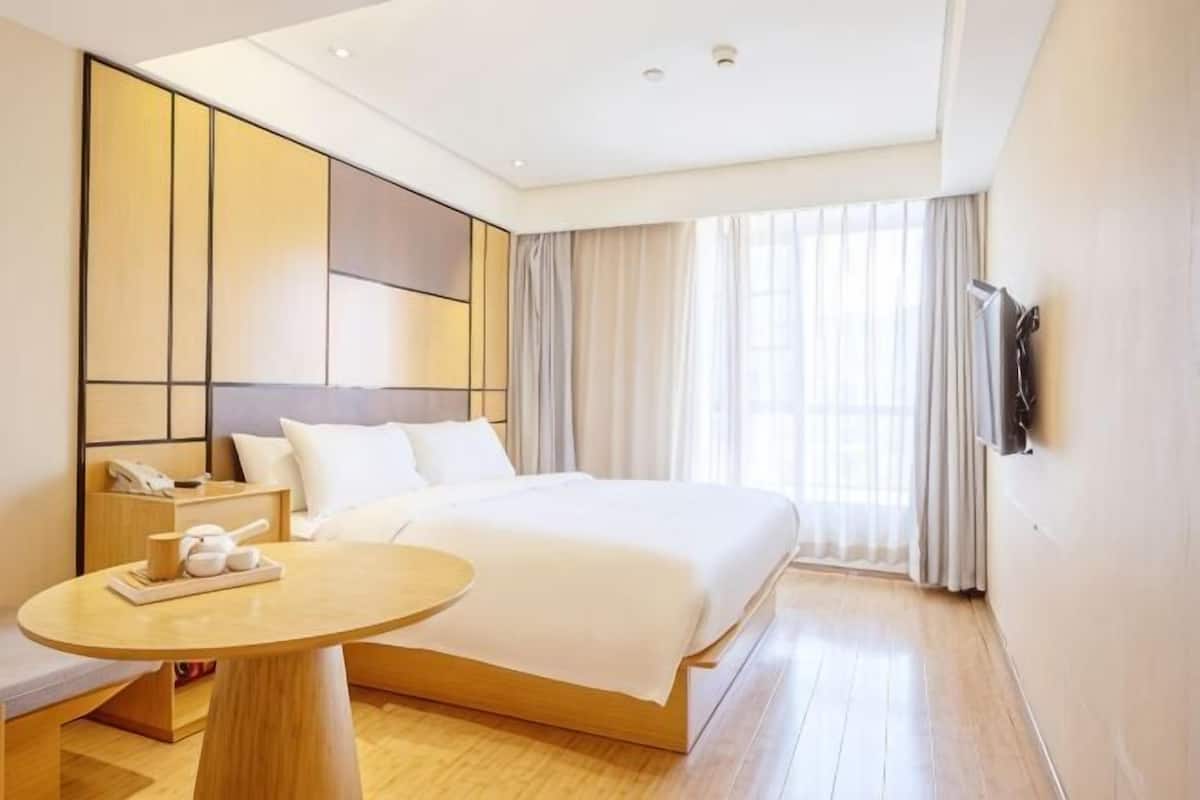 A hotel room with a large bed, bedside table, and a TV mounted on the wall.