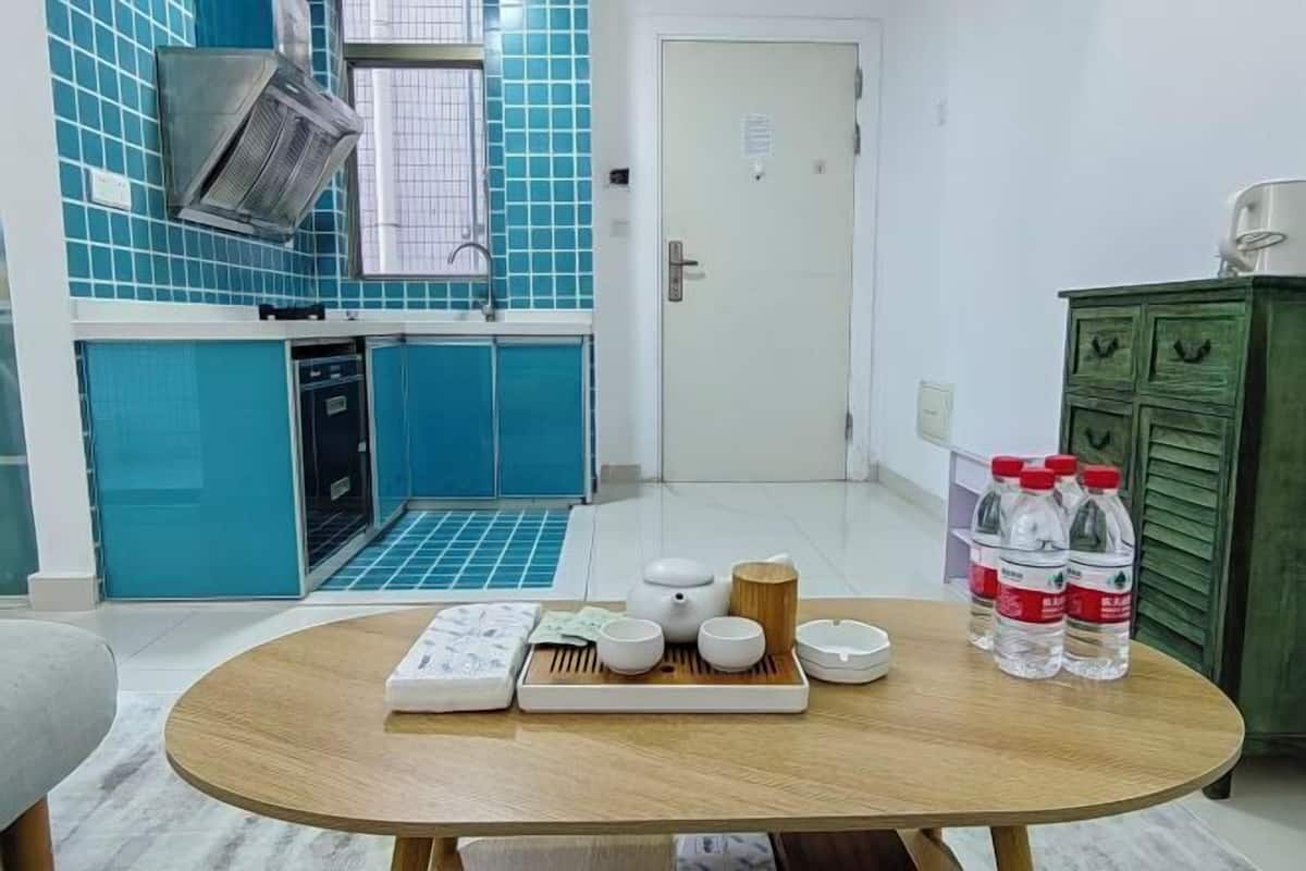 A compact kitchen with blue tiles, a green cabinet, and a table with tea set and bottled water.