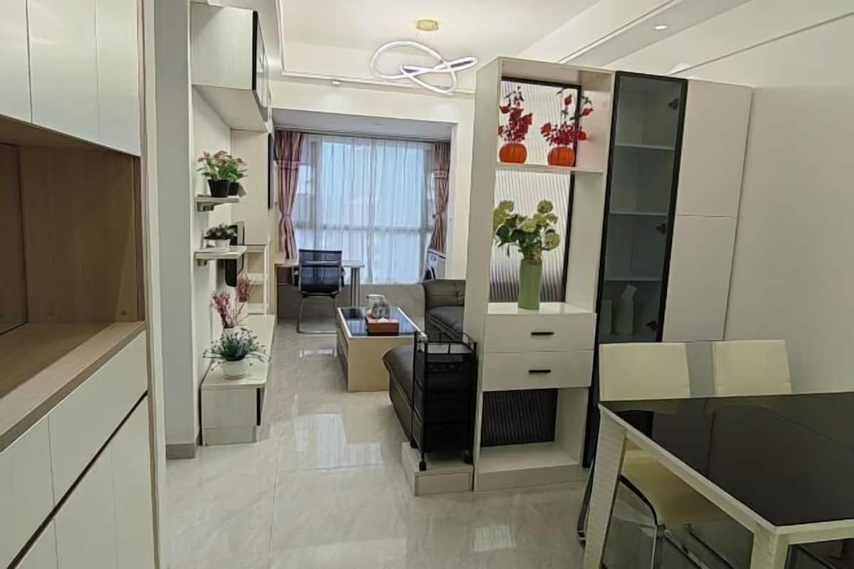 A modern kitchen with white cabinets, a dining area with a black table, and a living space with a sofa and TV.