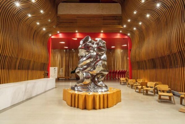 A modern interior with a central metallic sculpture on a wooden platform, surrounded by rows of wooden chairs. - Lilong hotel (Huizhou)