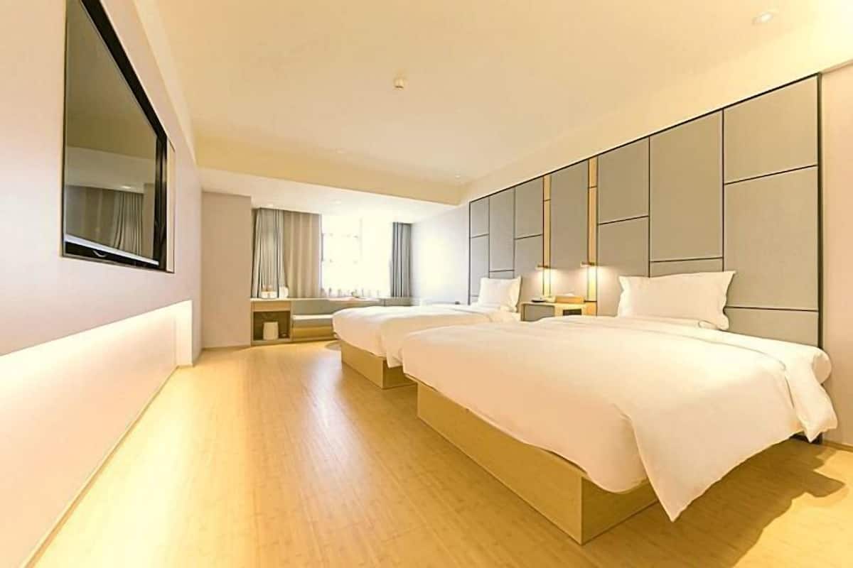 A hotel room with two beds, a large mirror, a bedside table with a lamp, and a view of the city.