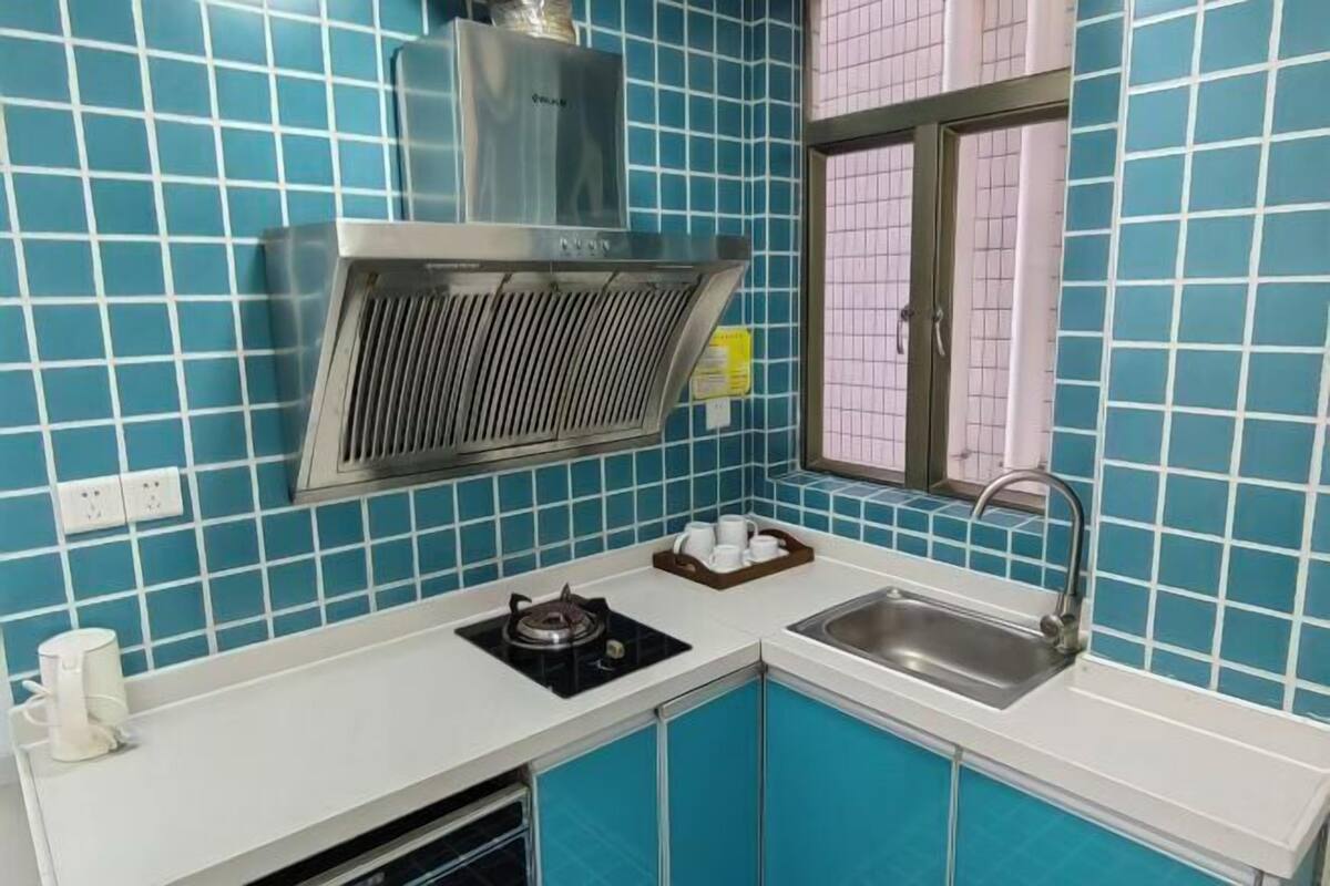 A kitchen with blue tiles, a stainless steel range hood, a gas stove, a sink, and a window with a grid pattern.