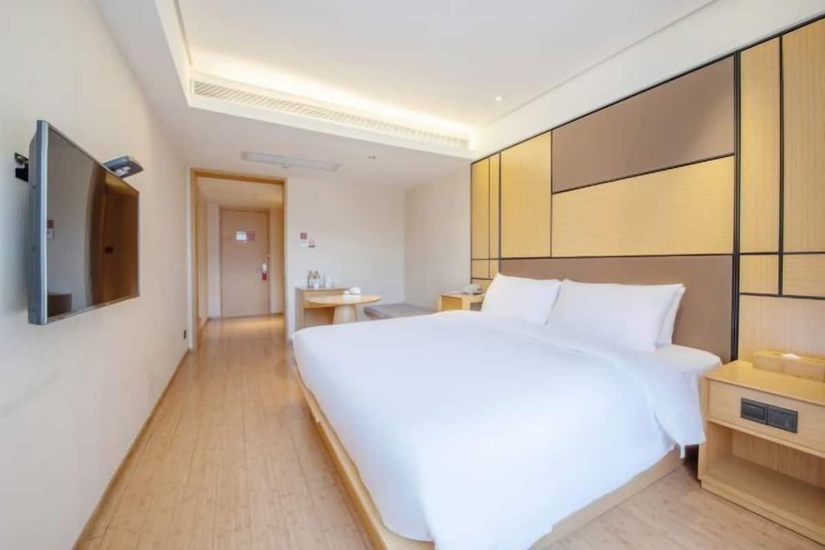 A modern hotel room with a large bed, a bedside table, a flat-screen TV mounted on the wall, and a wooden floor.