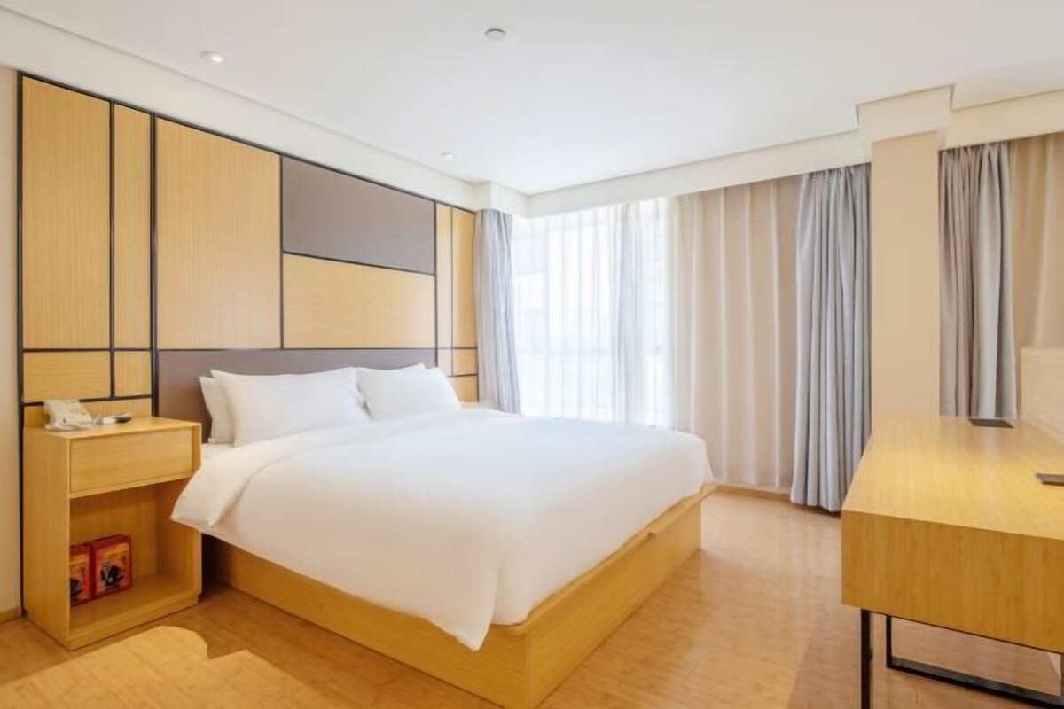 Ein modernes Hotelzimmer mit einem großen Bett, einem Holztisch und einem Nachttisch mit Lampe.
