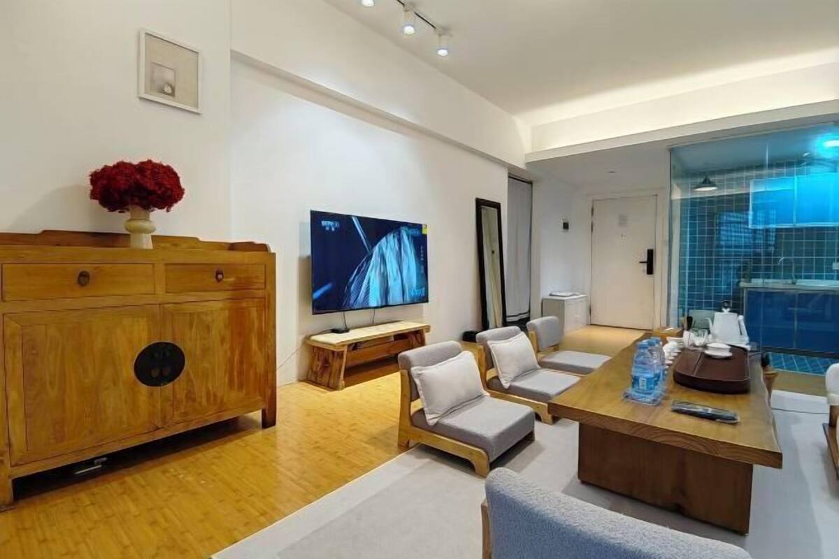 A modern living room with a wooden cabinet, a flat-screen TV, a dining table with chairs, and a blue-tiled area.