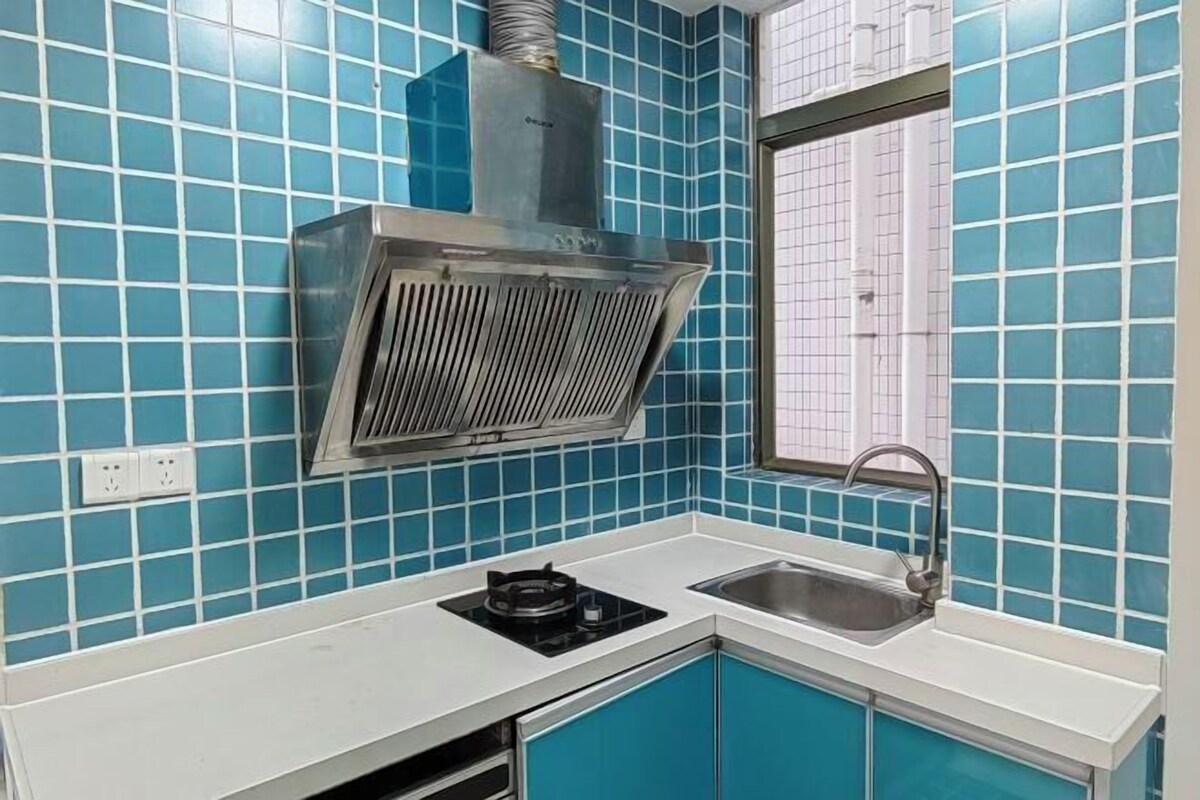 Eine Küche mit blauen Fliesen, einer Edelstahl-Dunstabzugshaube, einem Gasherd und einem Spülbecken.