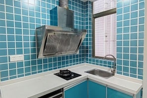 A kitchen with blue tiles, a stainless steel range hood, a gas stove, and a sink. - Lilong hotel (Huizhou)