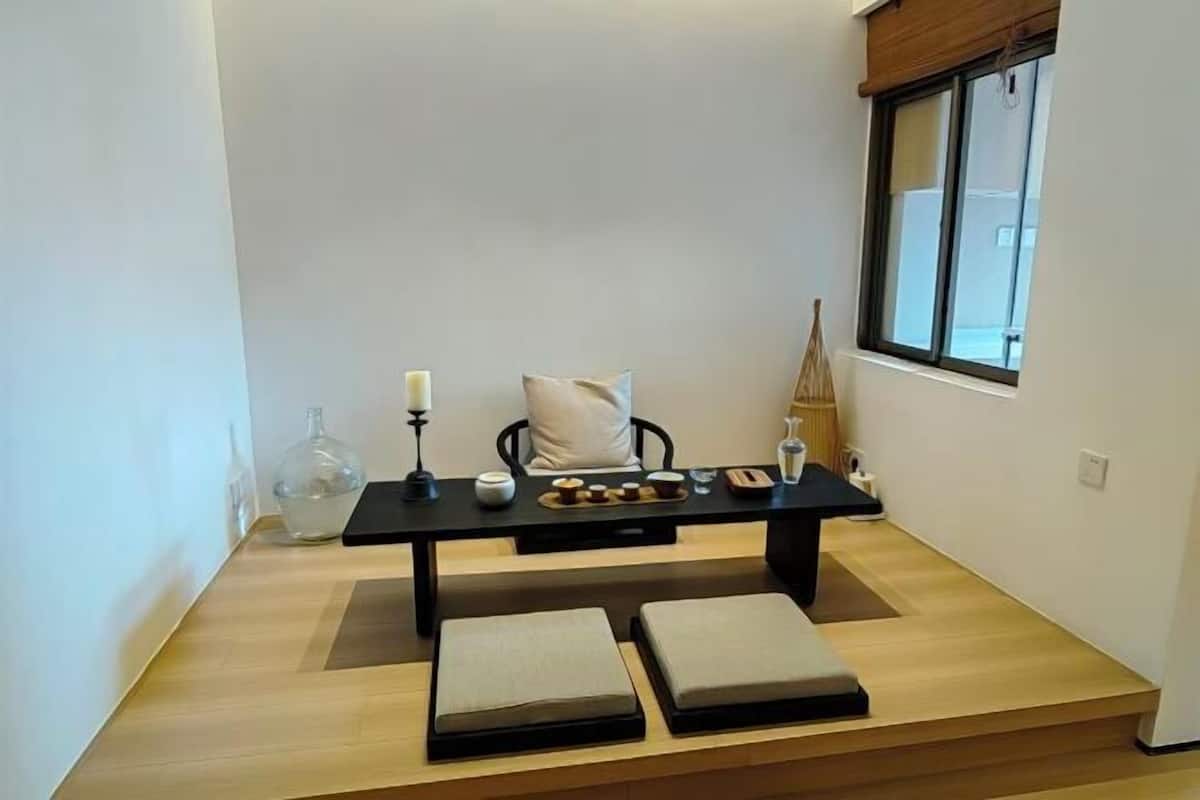 A small dining area with a table, cushions, a candle, and a window.