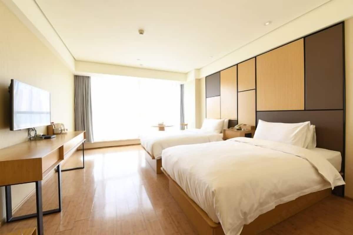 A hotel room with two beds, a desk, a television, and a large window.