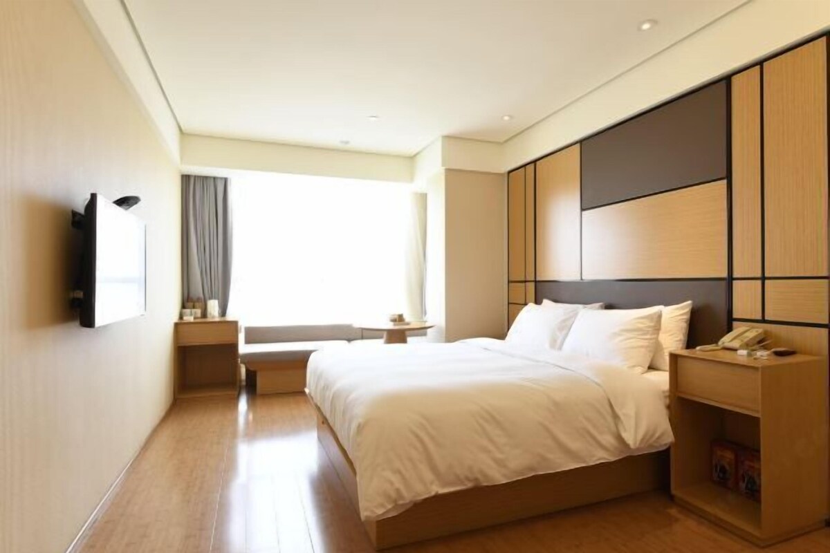 Ein modernes Hotelzimmer mit einem großen Bett, einem Nachttisch, einem Fernseher und einem Fenster mit Vorhängen.