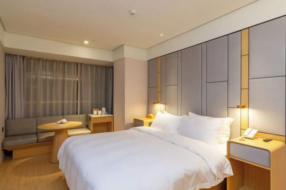 A hotel room with a bed, bedside tables, a round table, a sofa, and a large window with curtains.