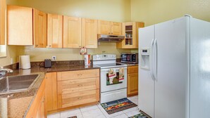 A kitchen with wooden cabinets, a white refrigerator, a stove, and a microwave. - Mins to the Coast: Port St Lucie Home w/ Lanai! (Fort Pierce)