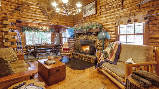 Interior de uma cabana de toras com lareira, móveis de madeira e uma placa indicando trilha de motos de neve.