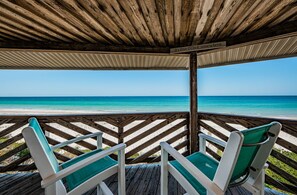 Une terrasse en bois avec deux chaises vertes dotées de coussins, donnant sur une plage.