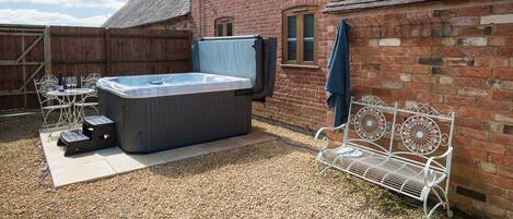 A backyard with a hot tub, a metal bench, and a wooden fence.
