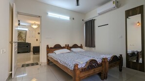 A bedroom with a wooden bed, a ceiling fan, an air conditioner, and a door leading to a living area. - Bed and Brew (Chennai)