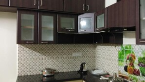 A kitchen with dark wooden cabinets, a microwave, a sink, and a tiled backsplash with a vegetable design. - Bed and Brew (Chennai)