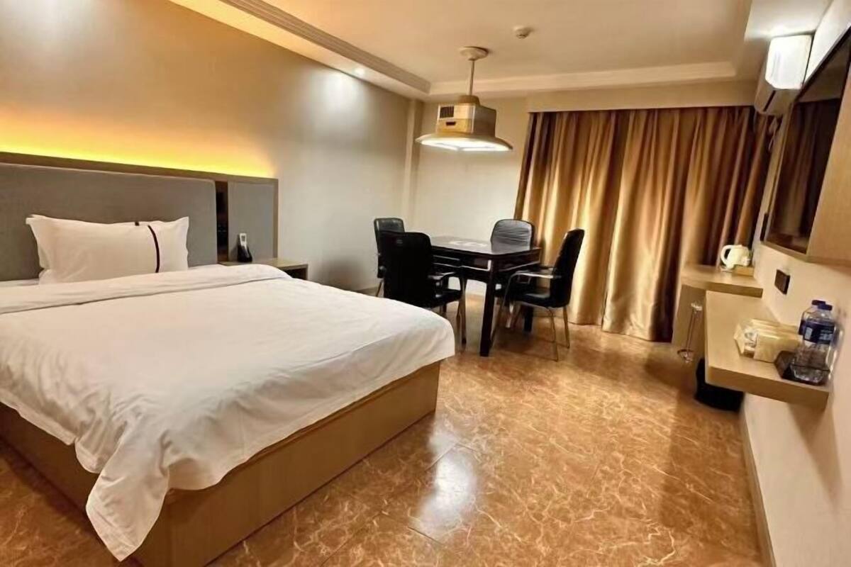 A hotel room with a large bed, a desk with two chairs, a small table with a lamp, and a minibar.