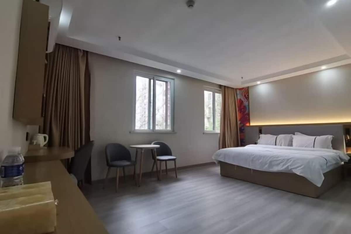 A hotel room with a bed, two windows, a desk with chairs, and a small table.