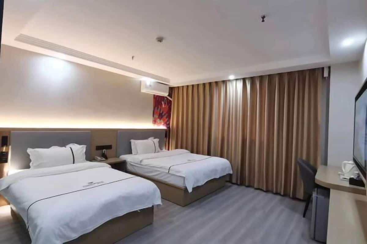 A hotel room with two beds, a desk, a chair, and a TV.