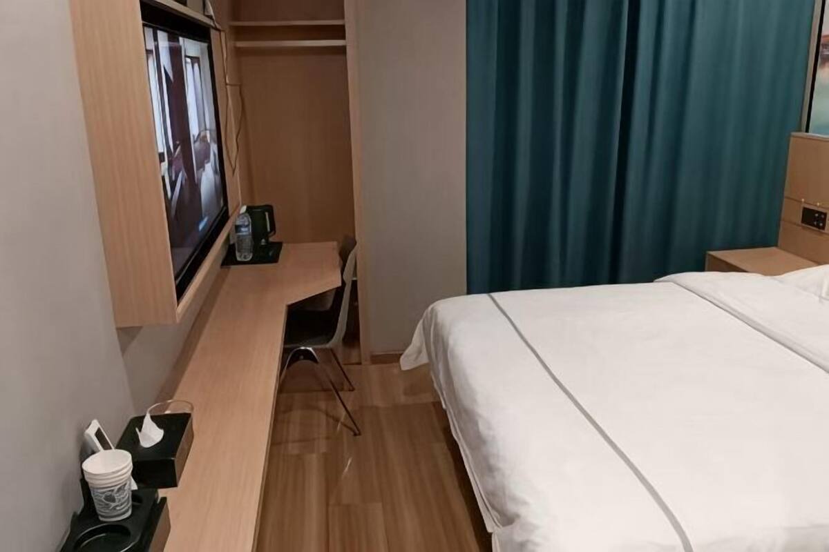 A hotel room with a bed, a desk, a TV, a closet, and a window with curtains.